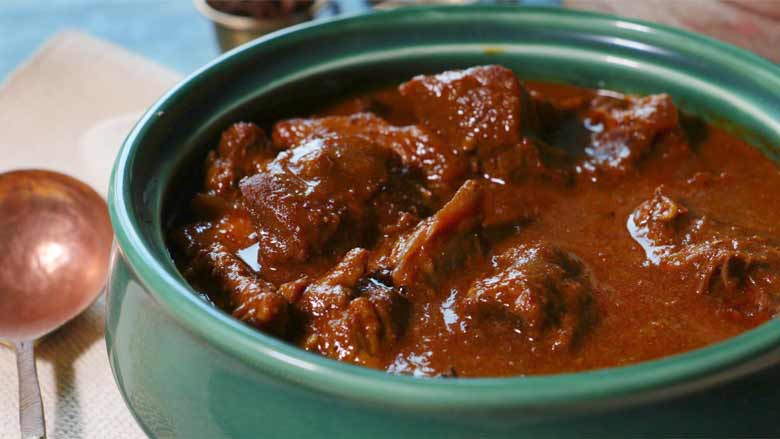 A closeup image of rich and glistening Rampuri Mutton Curry in an emerald green ceramic serving bowl with a copper ladle lying on the side - Taar Gosht Recipe
